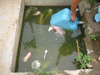 Eine Bewohnerin f�llt den Bidon mit
                        frischem Wasser, und der Bidon selbst ist im
                        total verschmutzten Wasser, Nahaufnahme